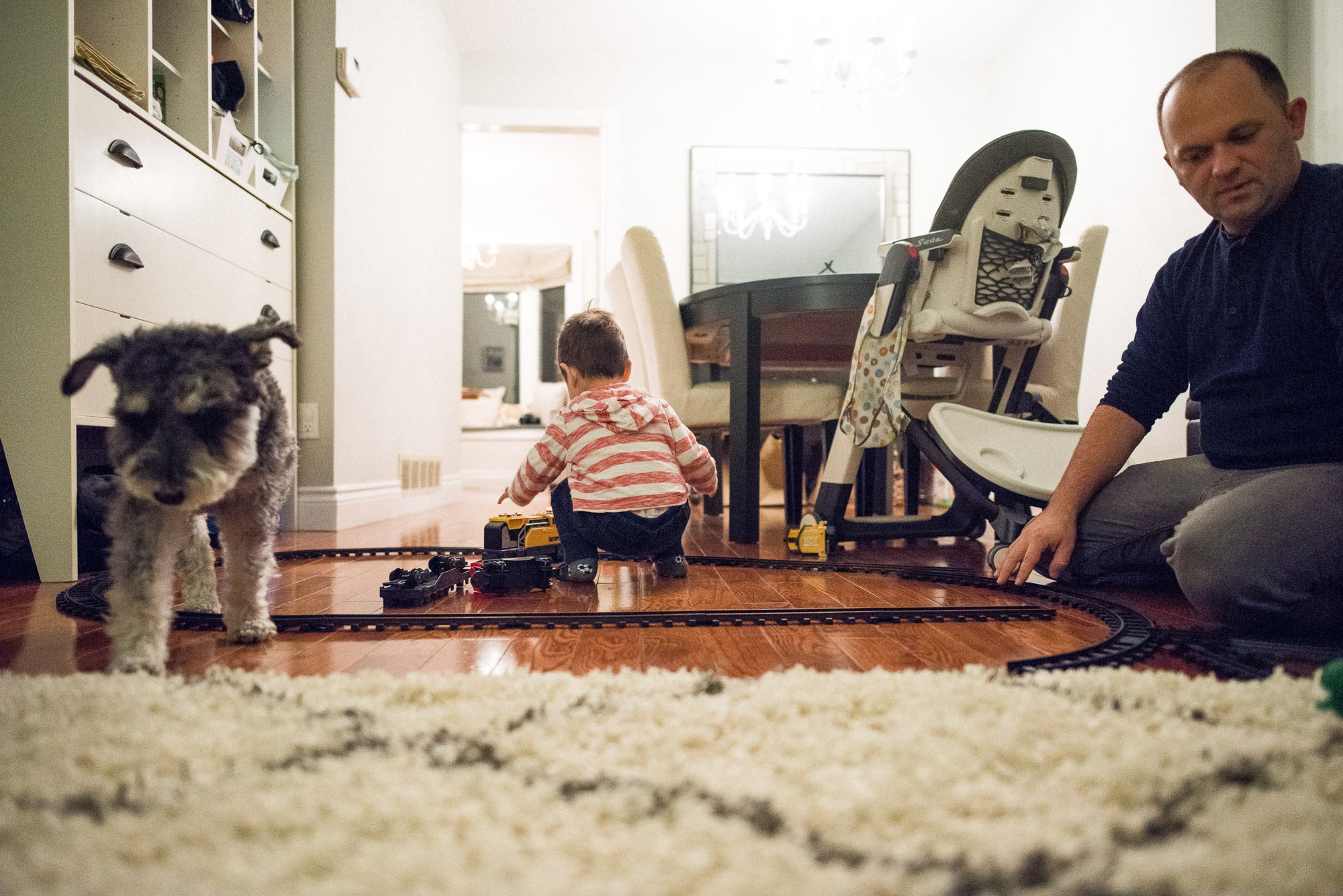 dad toddler and dog in the room with the toy train set