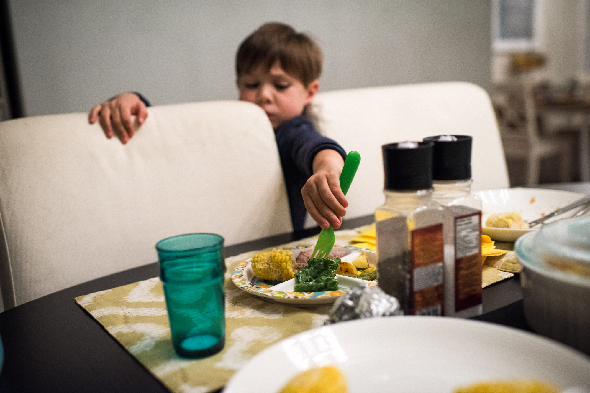 boy reaches between chairs to fork lettuce off a plate