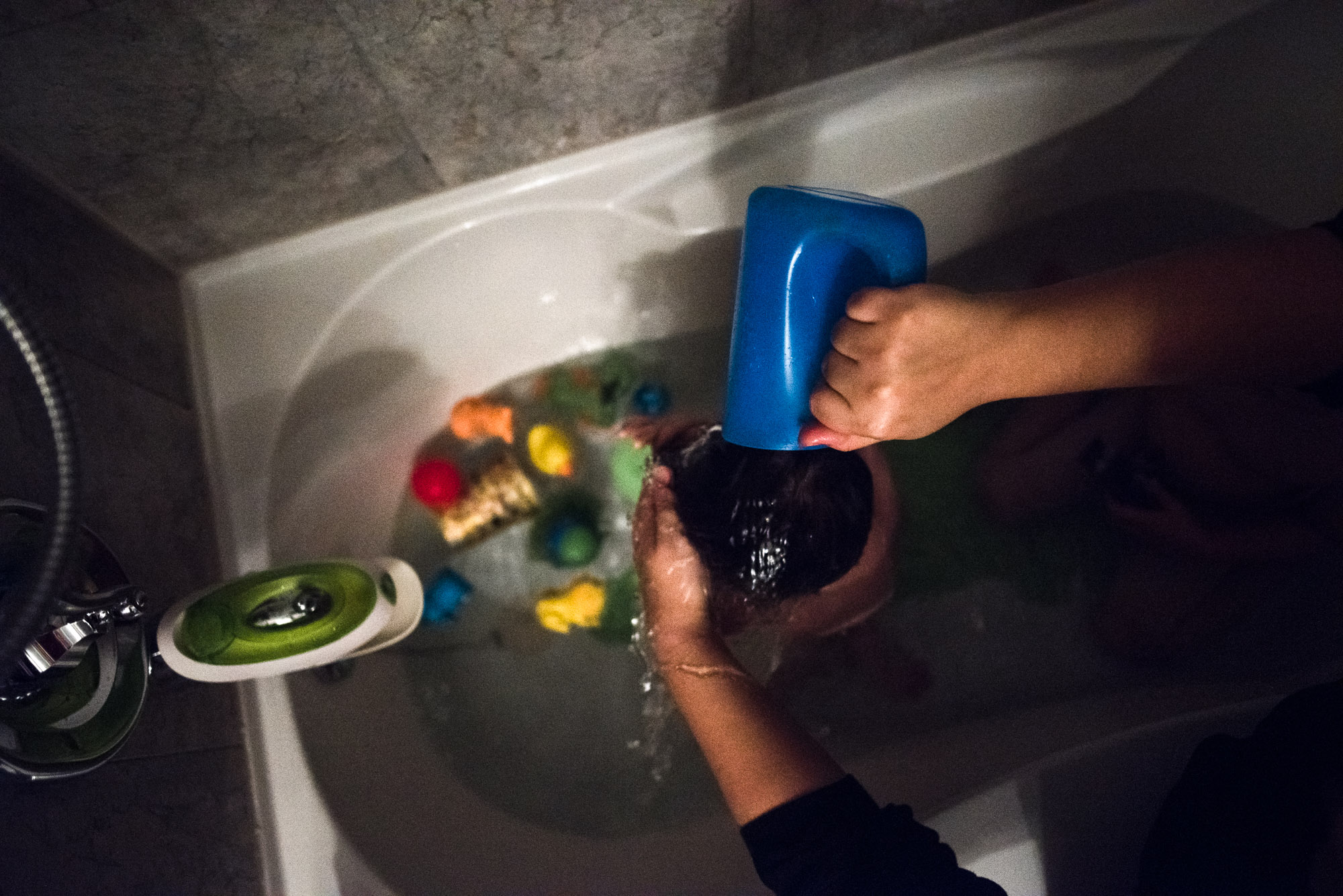 mom's hands pour water over boy's head in bathtub