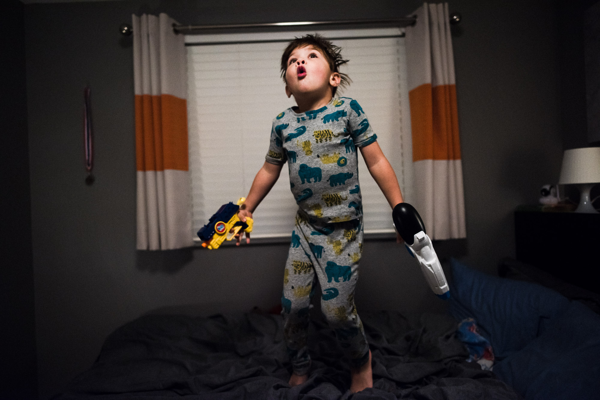 boy in PJs jumps on the bed with toy guns