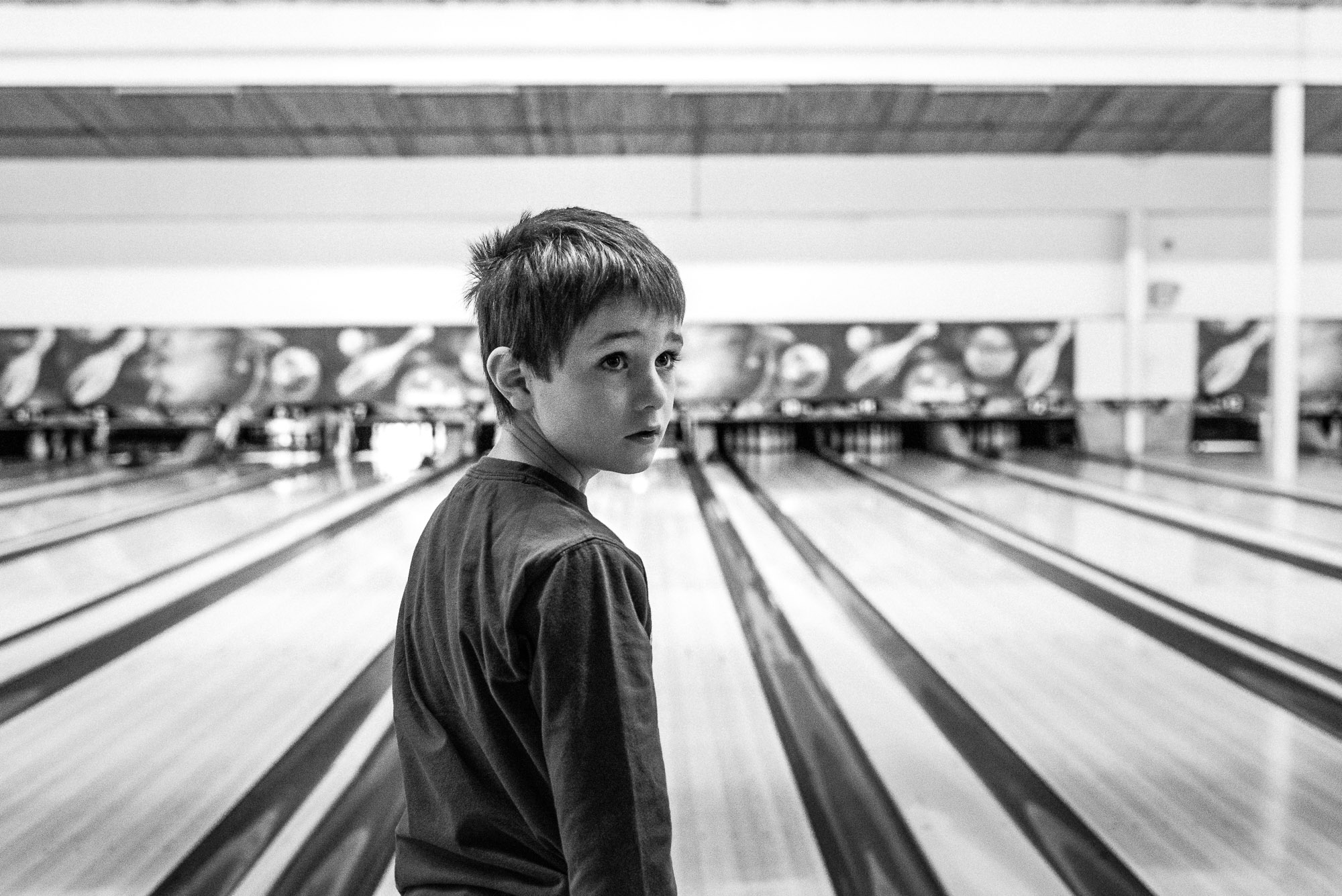 black and white photograph of boy looking back from a bowling alley