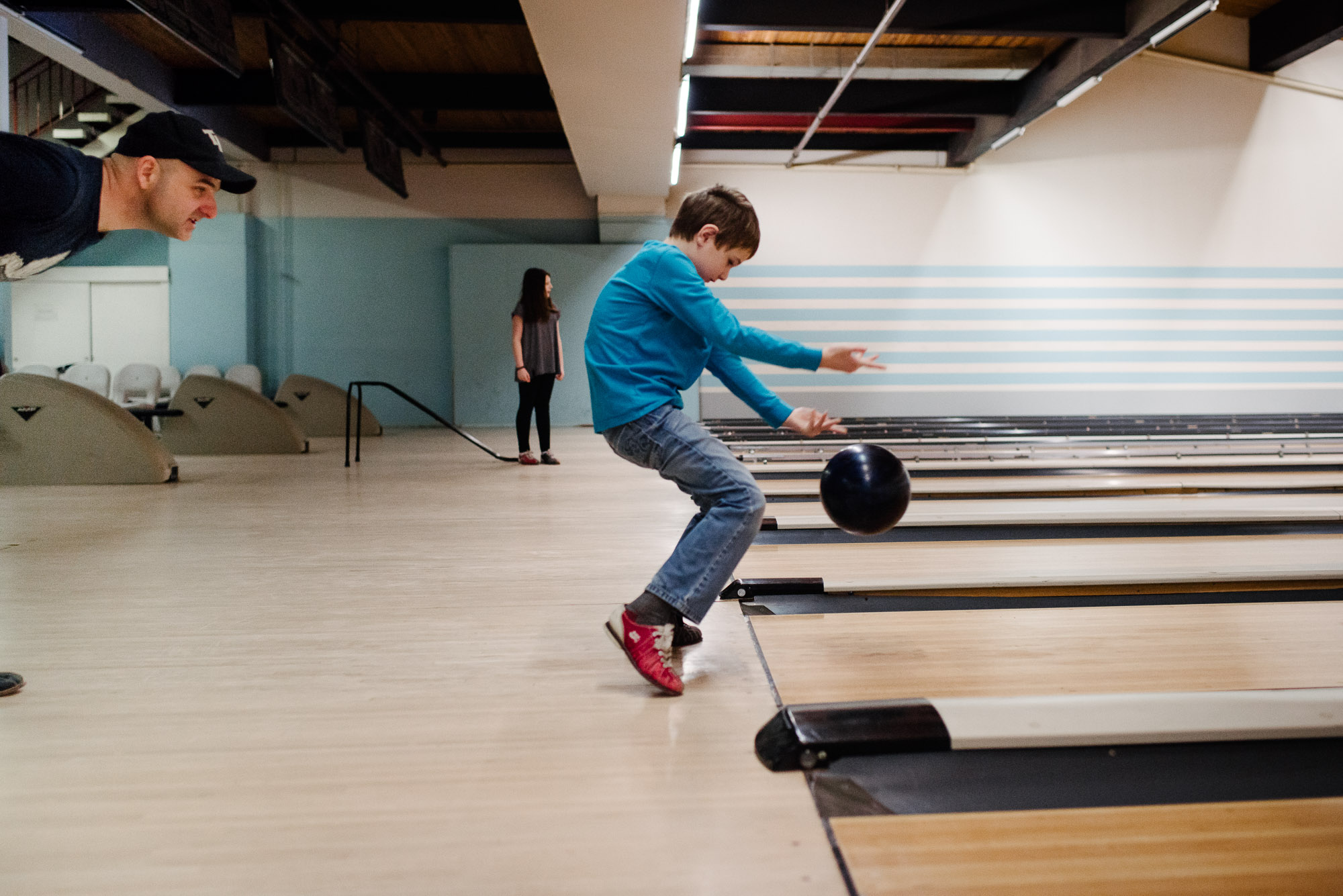 boy in blue shirts bowls as father watches on