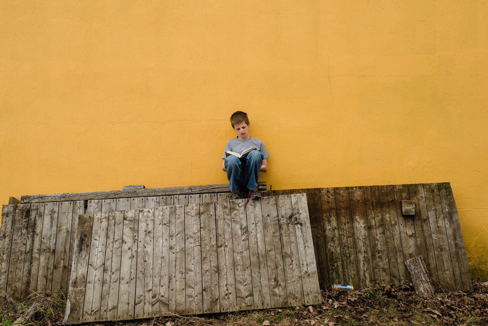 boy reads a book against a yellow wall