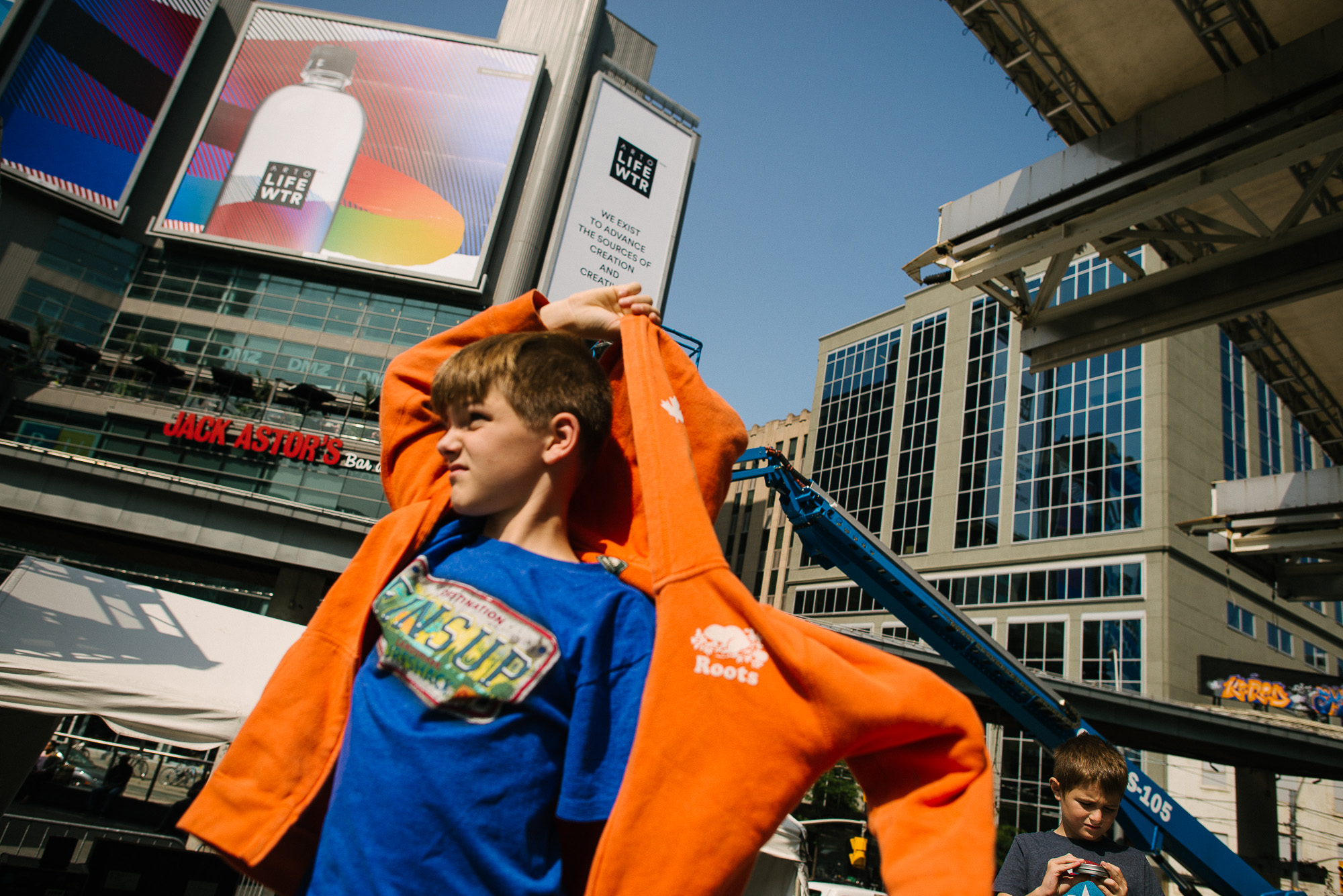 Boy with orange hooded sweatshirt stands in Dundas Square