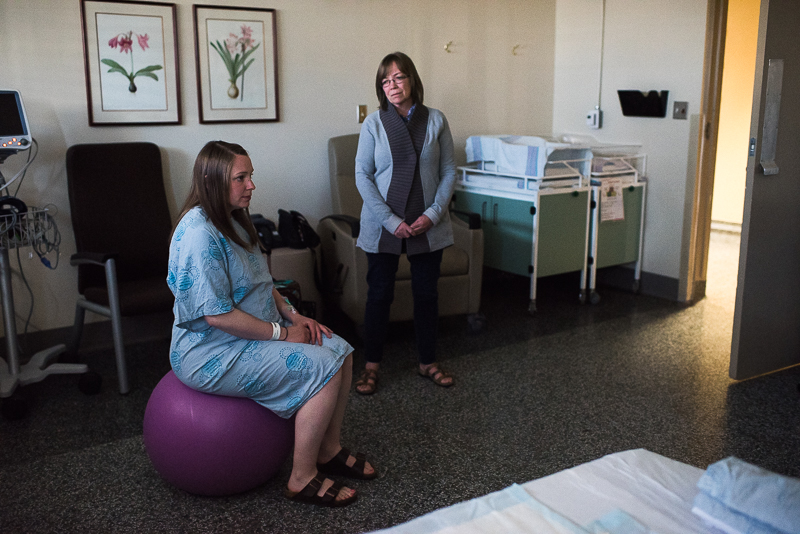 labouring mother sits on inflatable ball as her mother watches her in hospital delivery room