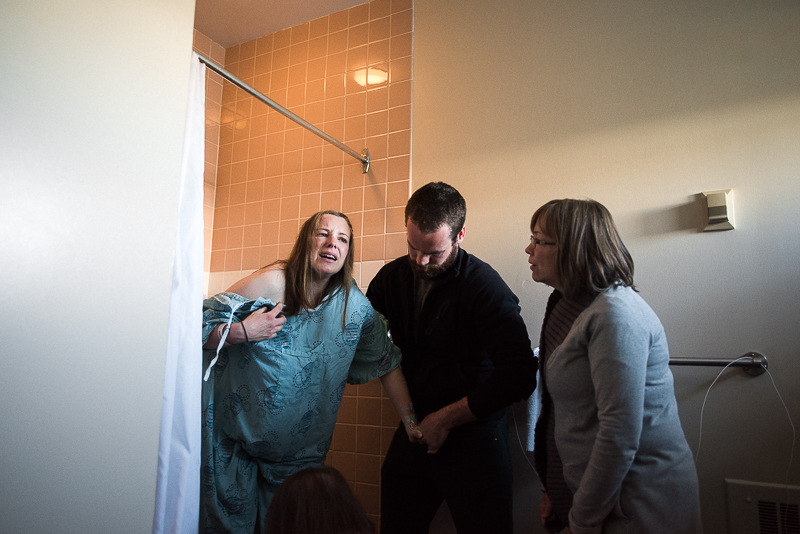 husband and mother help labouring woman exit the shower during a painful contraction