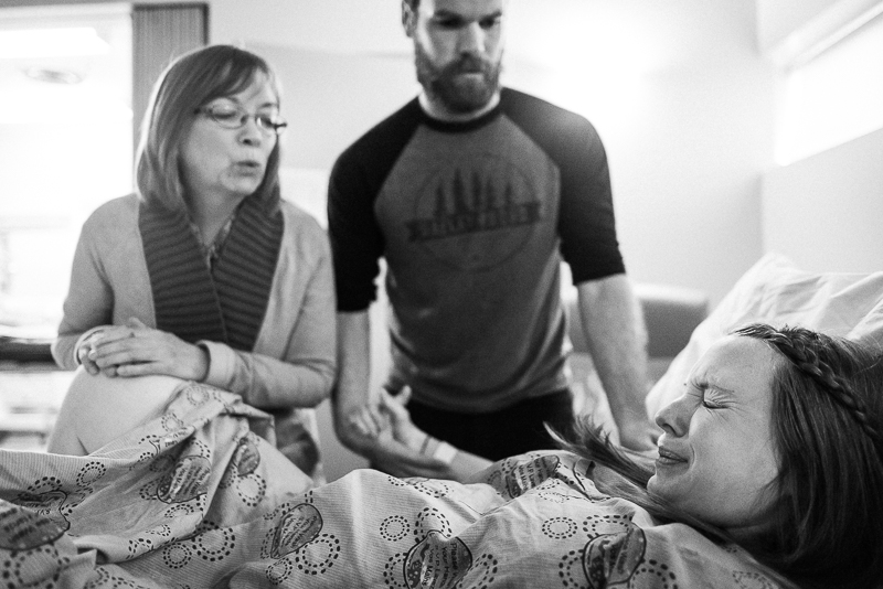 labouring woman pushes through a contraction watched by her husband and mother