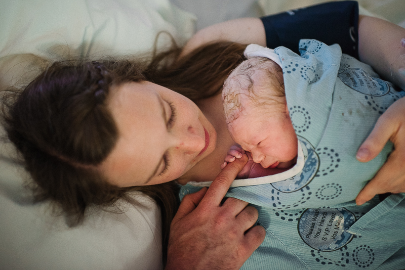 baby lies on mother's chest and holds father's finger