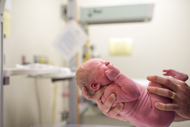male obstetrician hands hold newborn baby for weighing