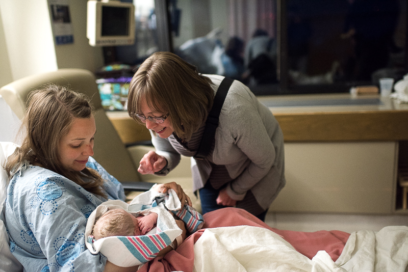 grandmother peeks at newborn grandson in her daughter's arms