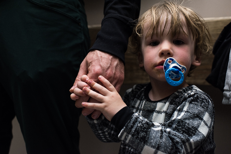 little boy with a soother clutches his father's hand