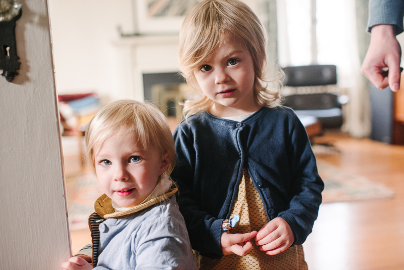 two young sisters look out from the doorway at a documentary family photography session in ottawa