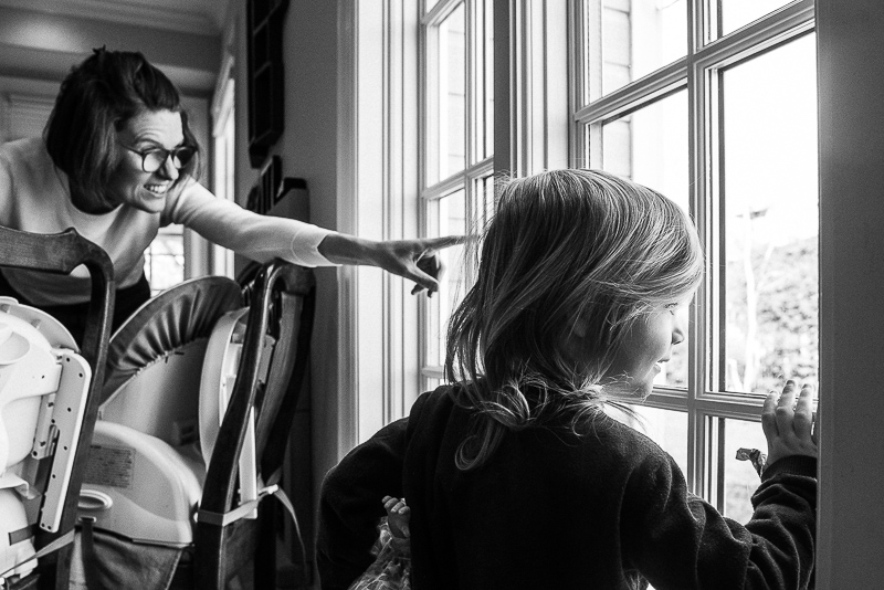 black and white photograph of mother and daughter looking outside the window during documentary family photography session in ottawa