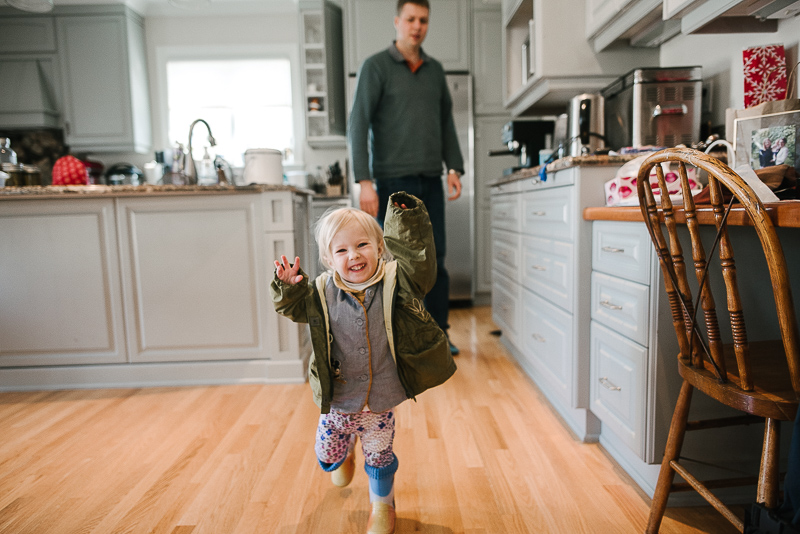 young girl in green jacket runs smiling in the kitchen during ottawa family photography session