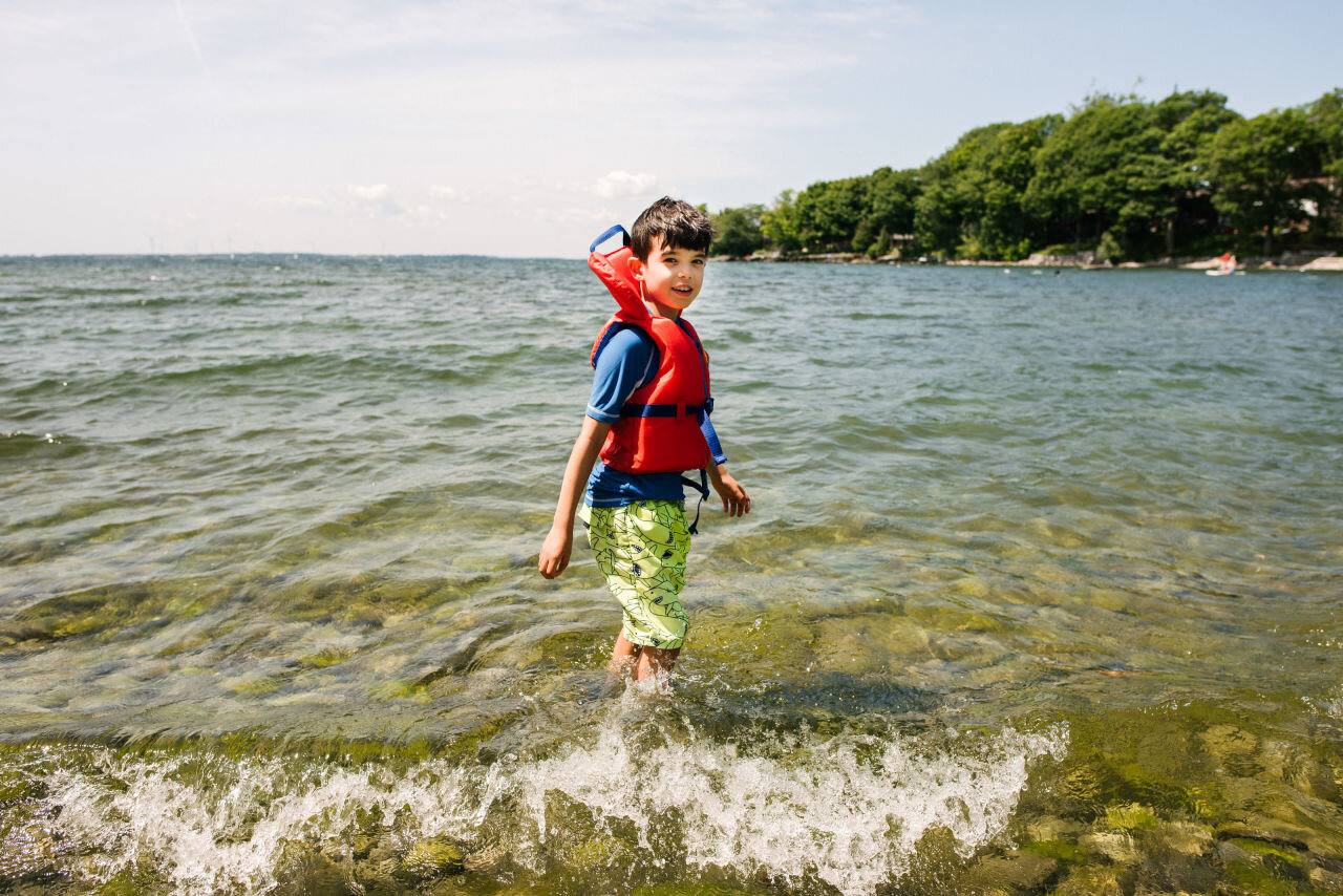 Young man going swimming in Lake Ontario during a family photography session in Kingston, Ontario 