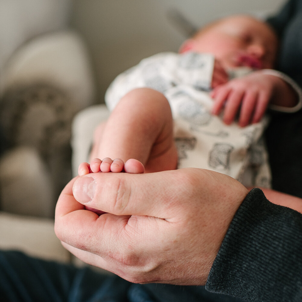 details of little newborn baby toes held by daddy's hand