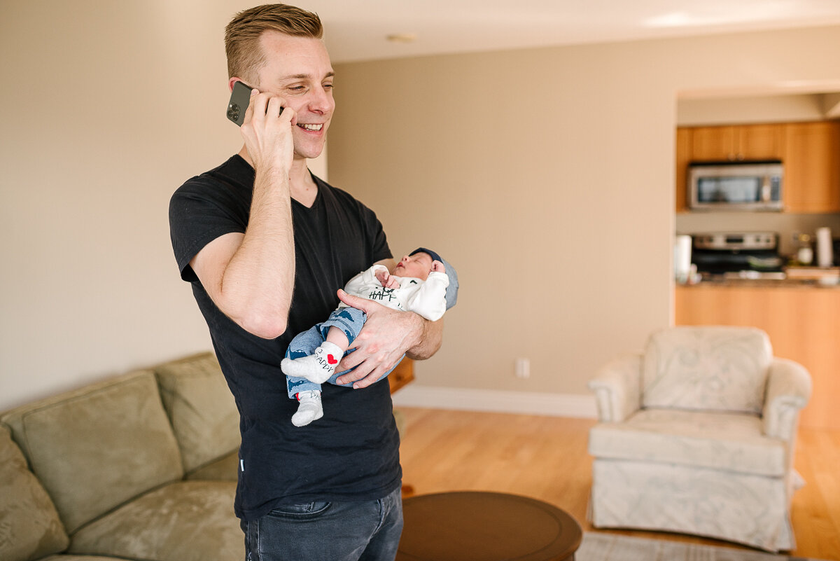 Dad holding new baby while on the phone sharing the news in kingston 