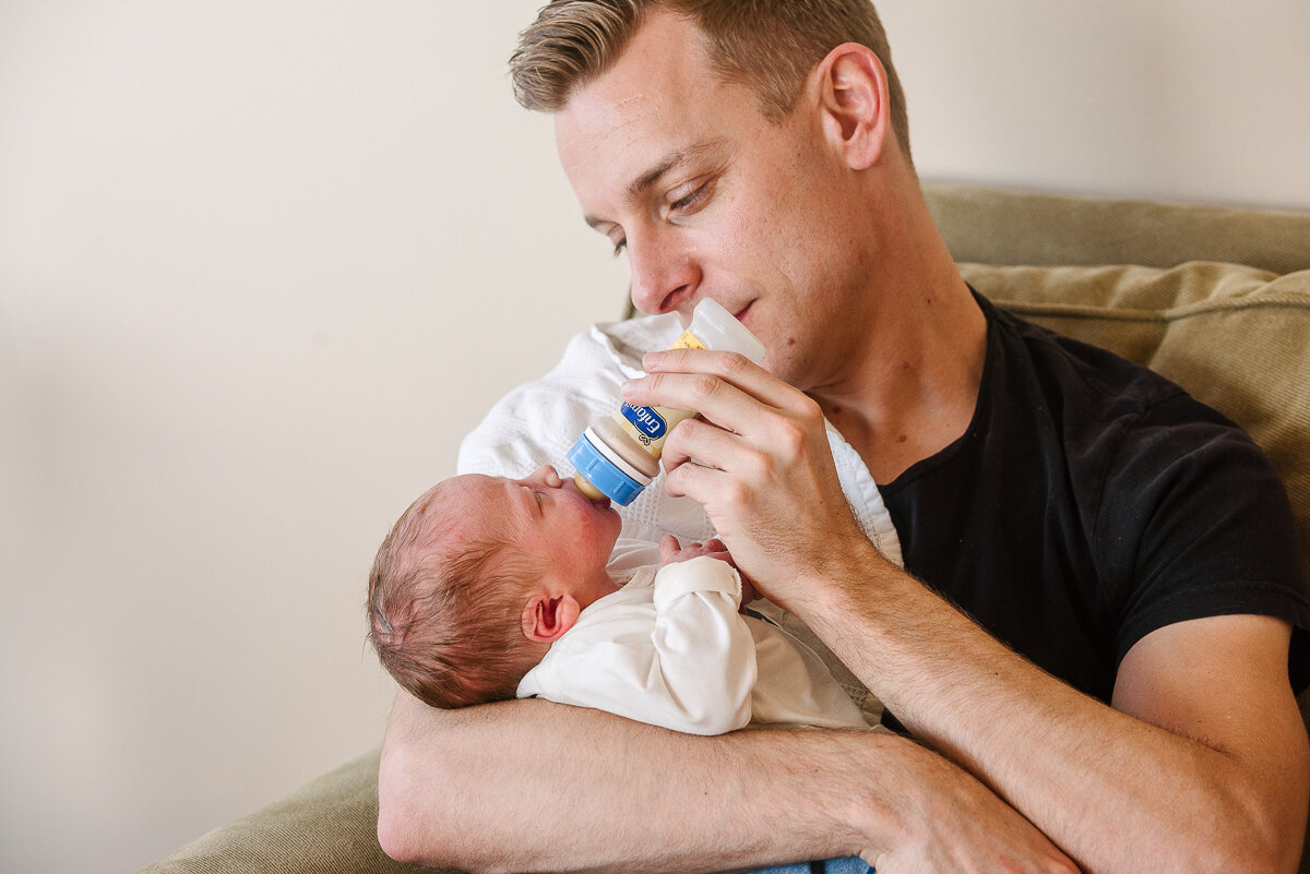 dad holding new born baby and feeding him a bottle 