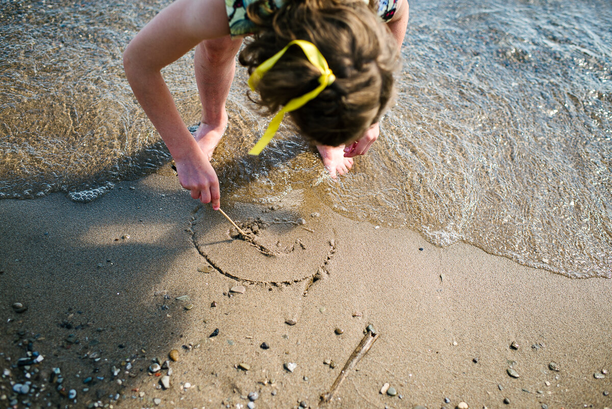 little girl draws in the sand at a beach in Toronto  