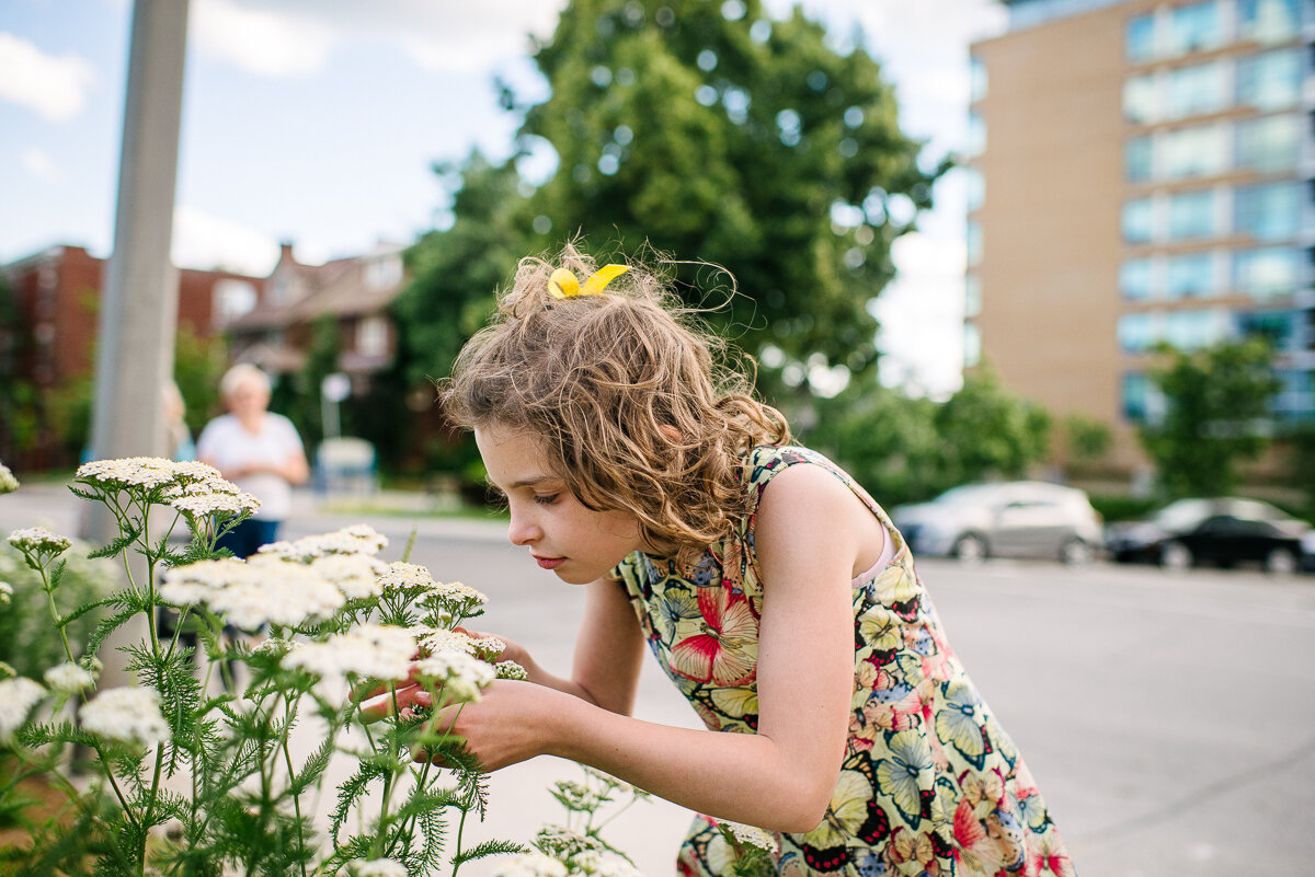 girl stopping to smell the flowers on the walk home in Toronto 