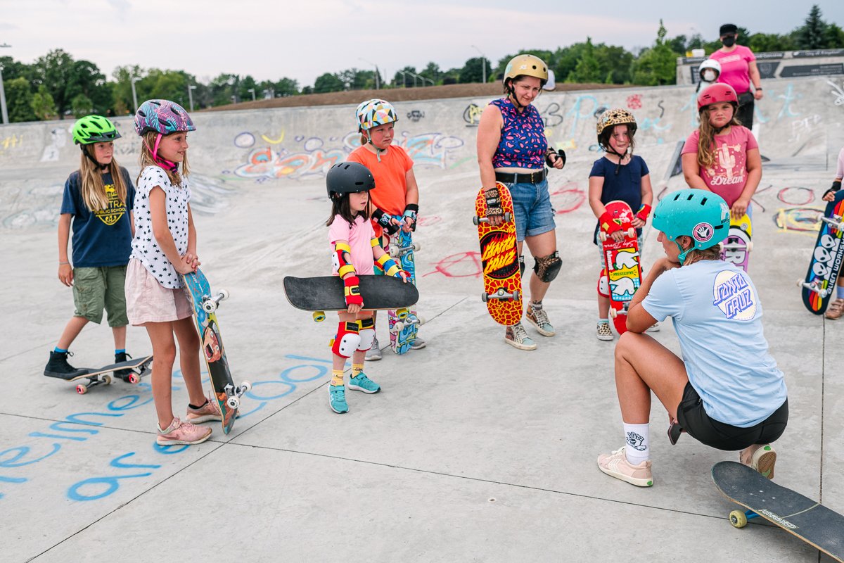Girls wearing helmet and holding skateboards.