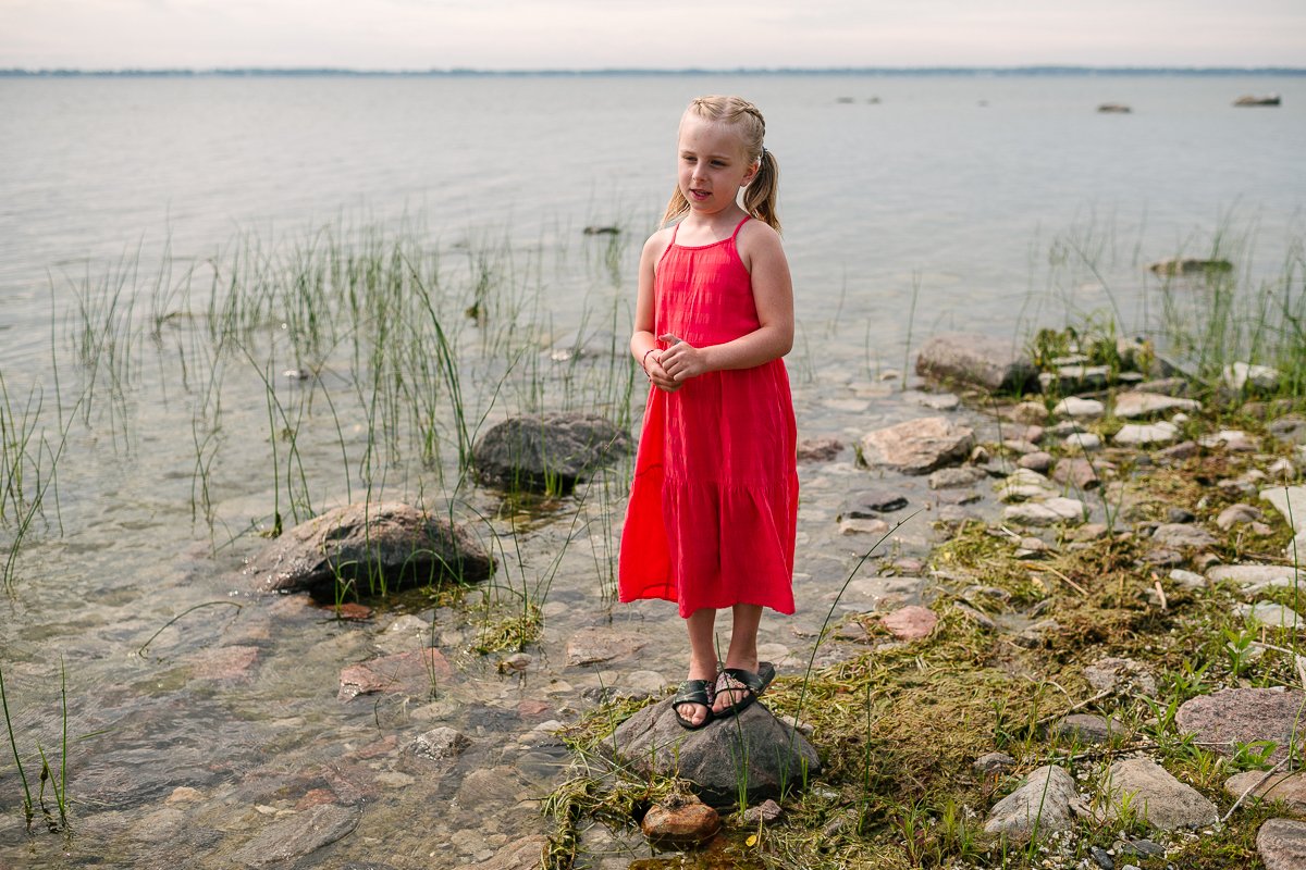 Girl wearing orange dress is playing near the lake. 