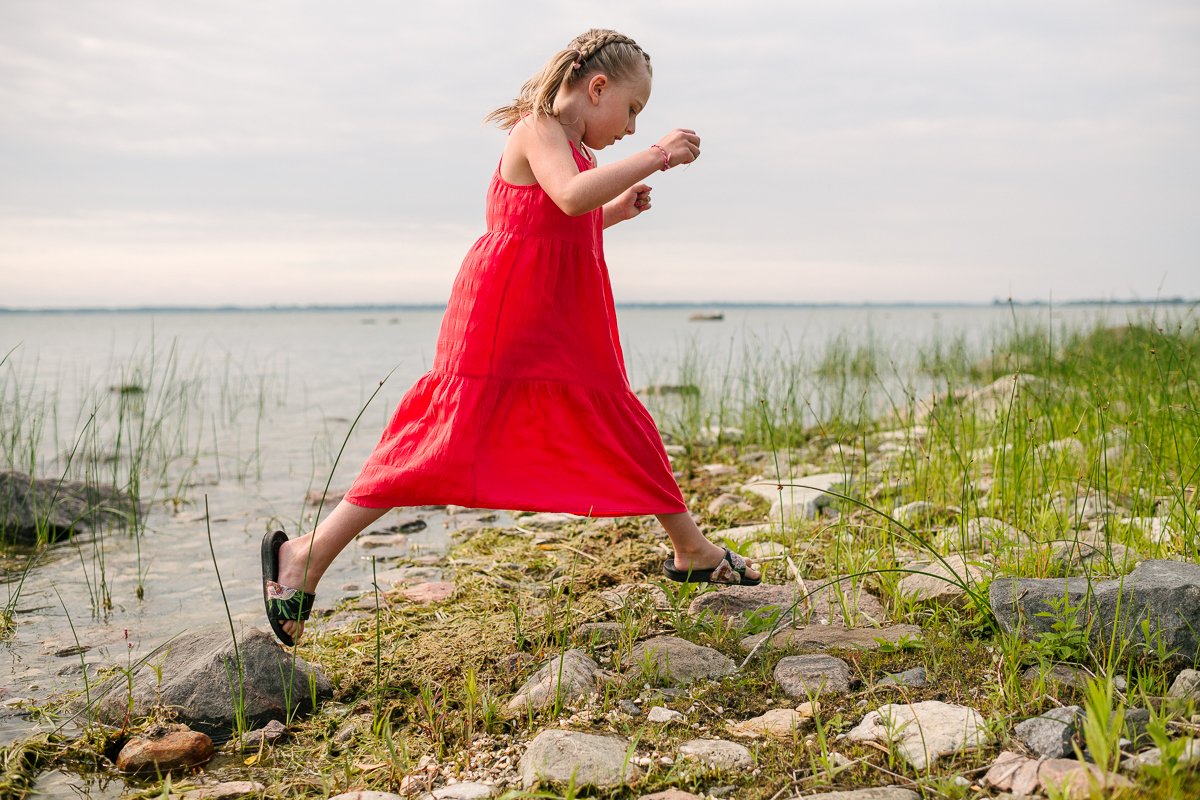 Girl wearing orange dress is playing near the lake. 