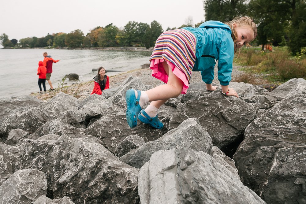 Little girl climbing up the rocks with excitement near the lake