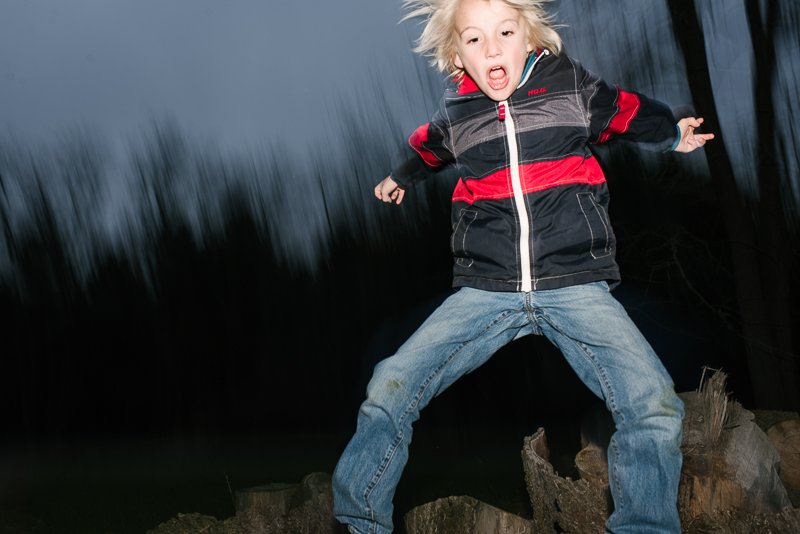 Young boy jumping in the night in the garden while playing. 