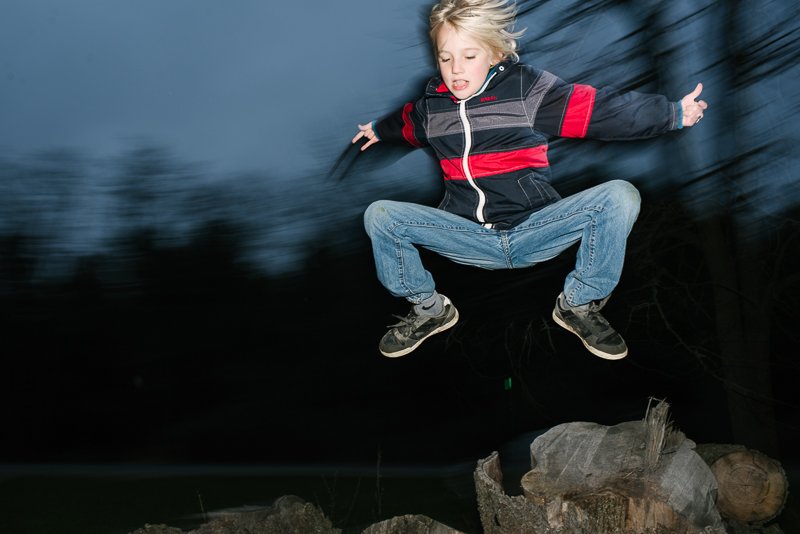 Young boy jumping in the night in the garden while playing. 