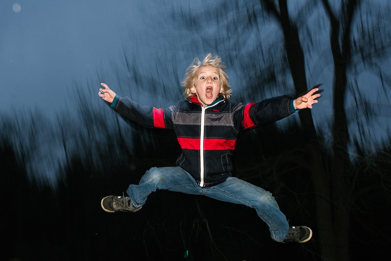 Young boy jumping in the night in the garden while playing. 