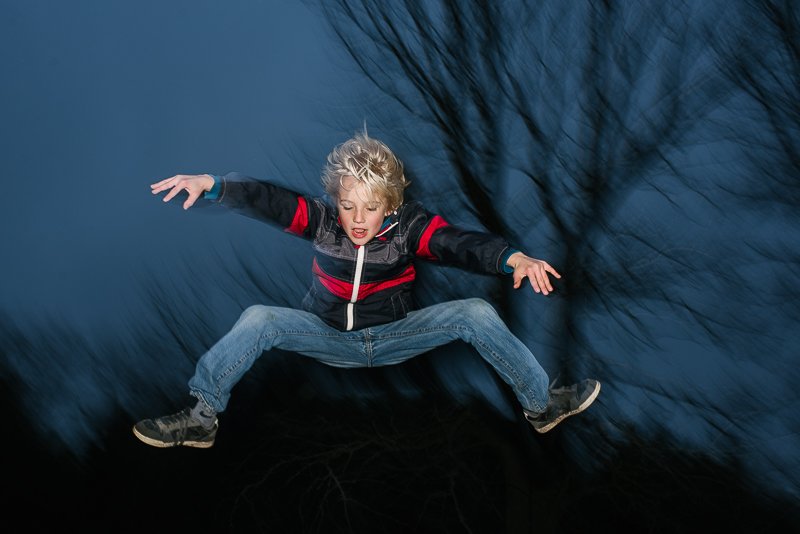 Young boy jumping in the night in the garden while playing. 