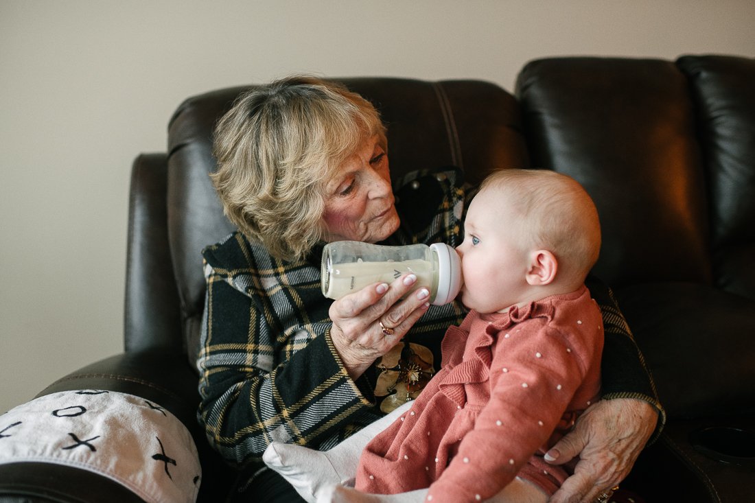 Grand mother feeding her new born grand daughter with bottle holding her in arms. 