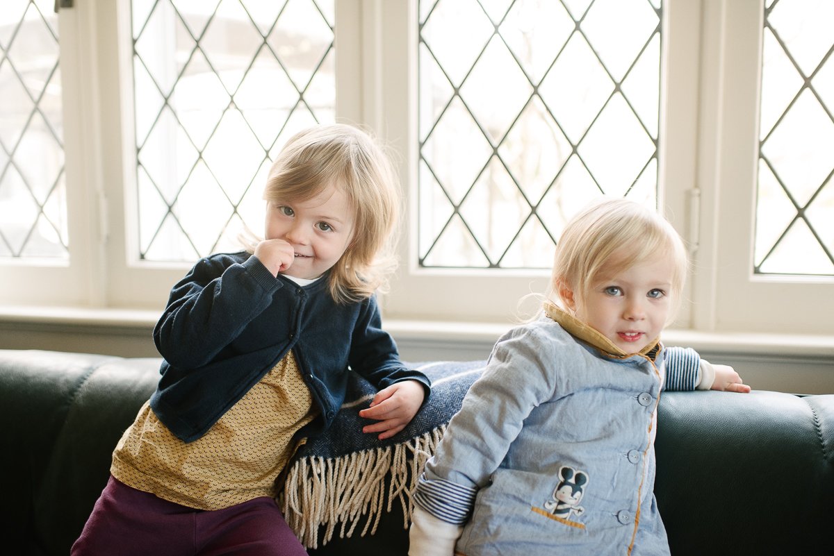 Little Girls with blonde hairs wearing blue coats sitting on sofa 