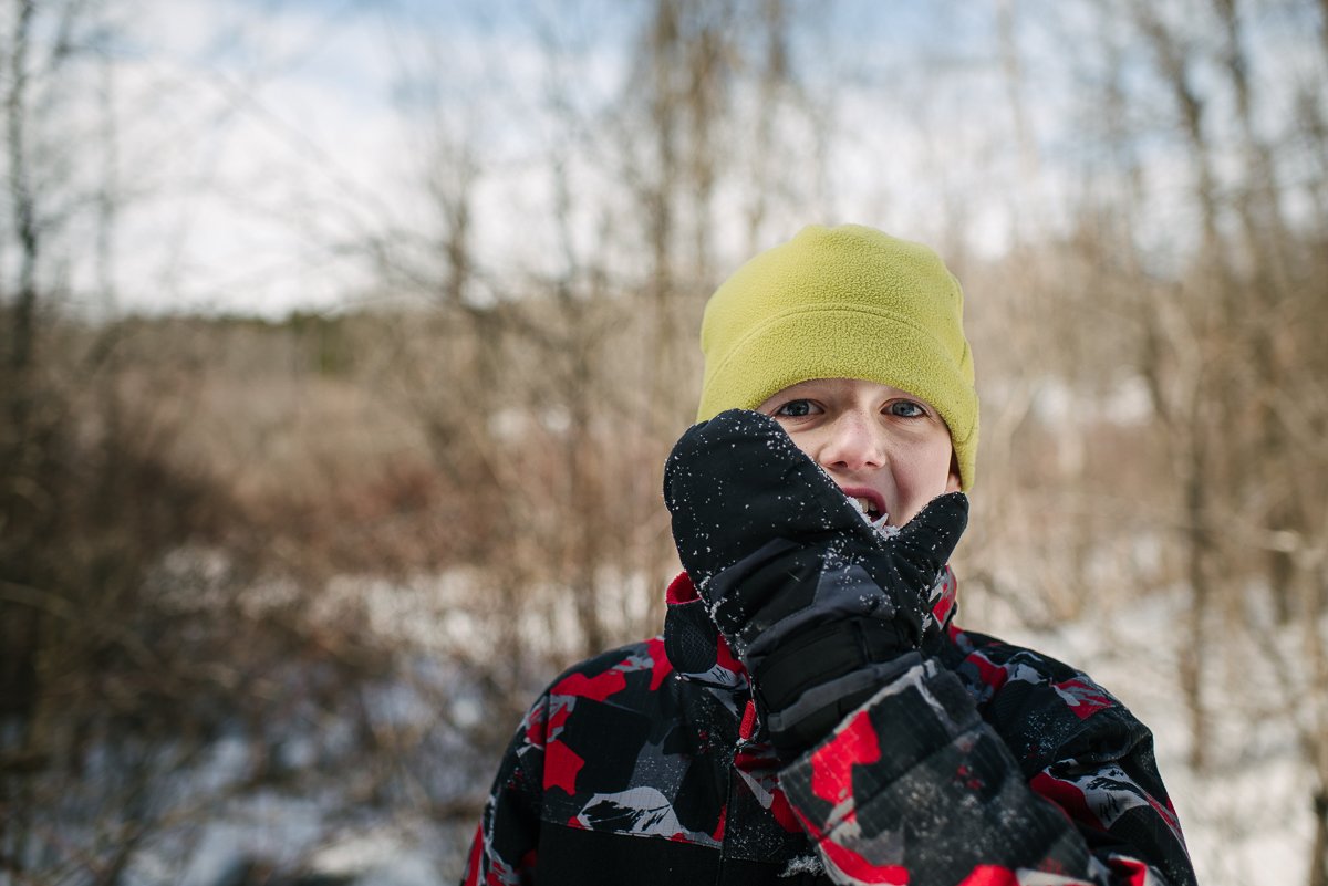 Boy wearing yellow winter cap and black jacket playing in snow at the park.