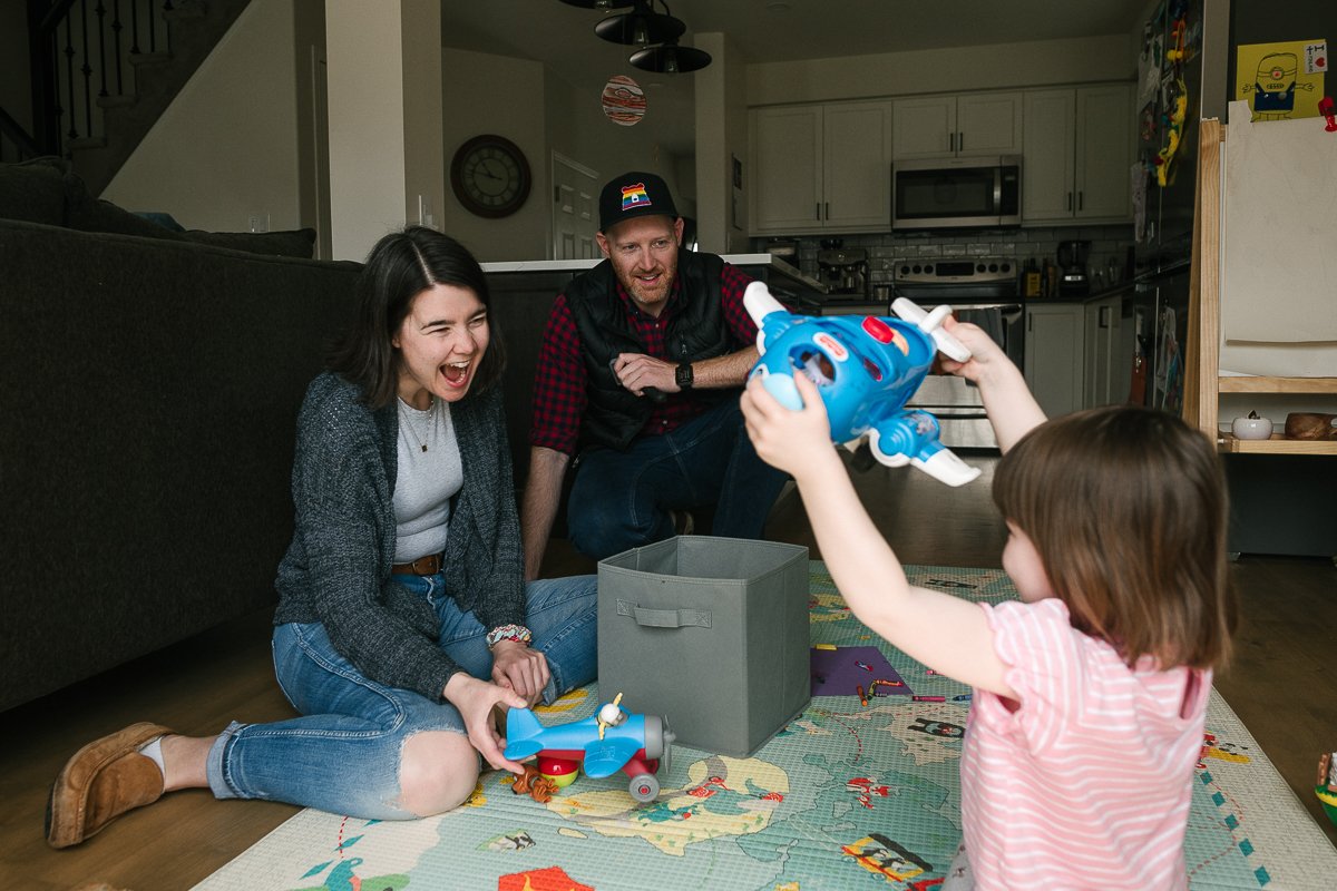 Mom dad playing with their daughter in the living area.