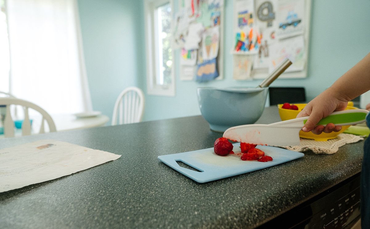 Boy cutting strawberry with a knife.