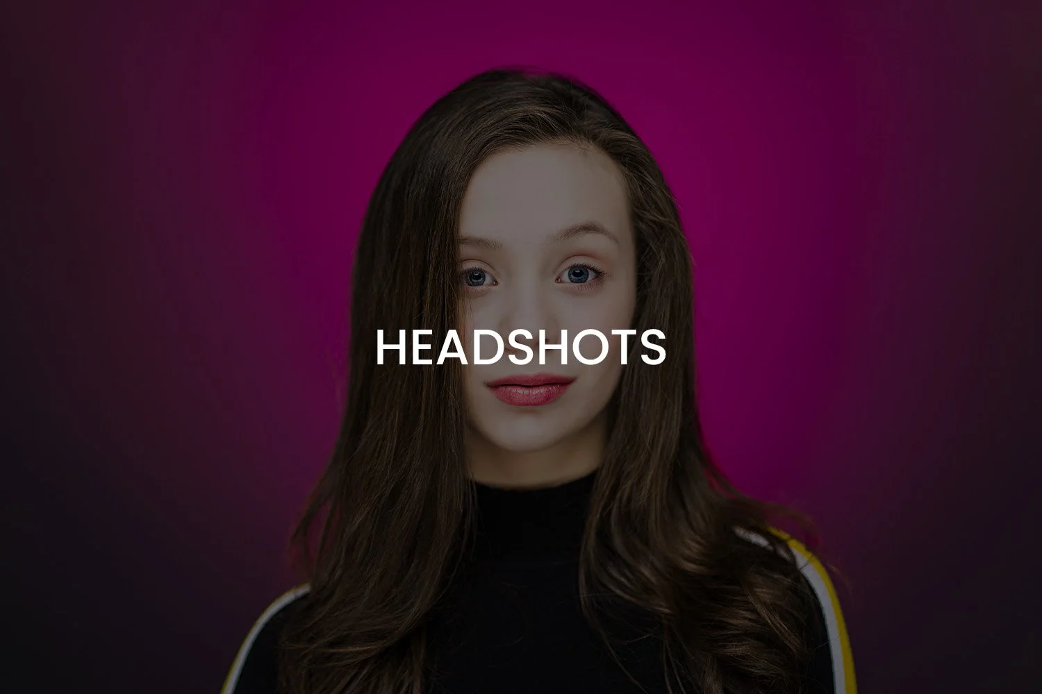 A young woman with long brown hair, blue eyes, and fair skin, wearing a black top with white and yellow stripes on the shoulders, standing against a gradient pink and purple background.