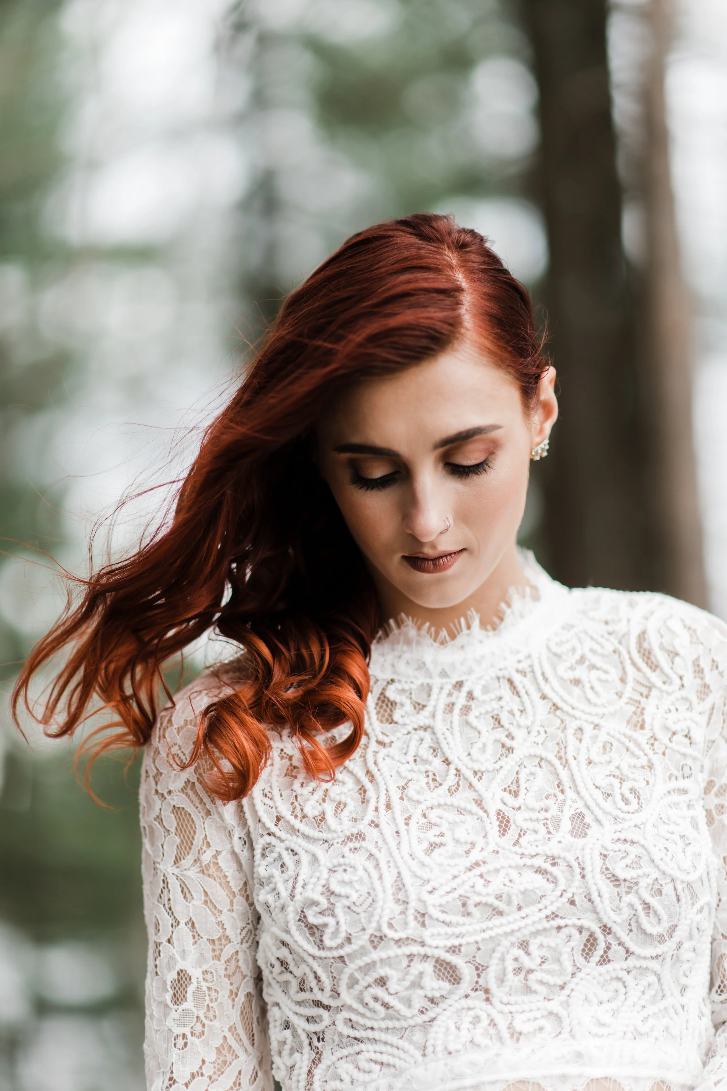 Bride looking down in lace and beaded crop top with red curly hair blowing in the wind.