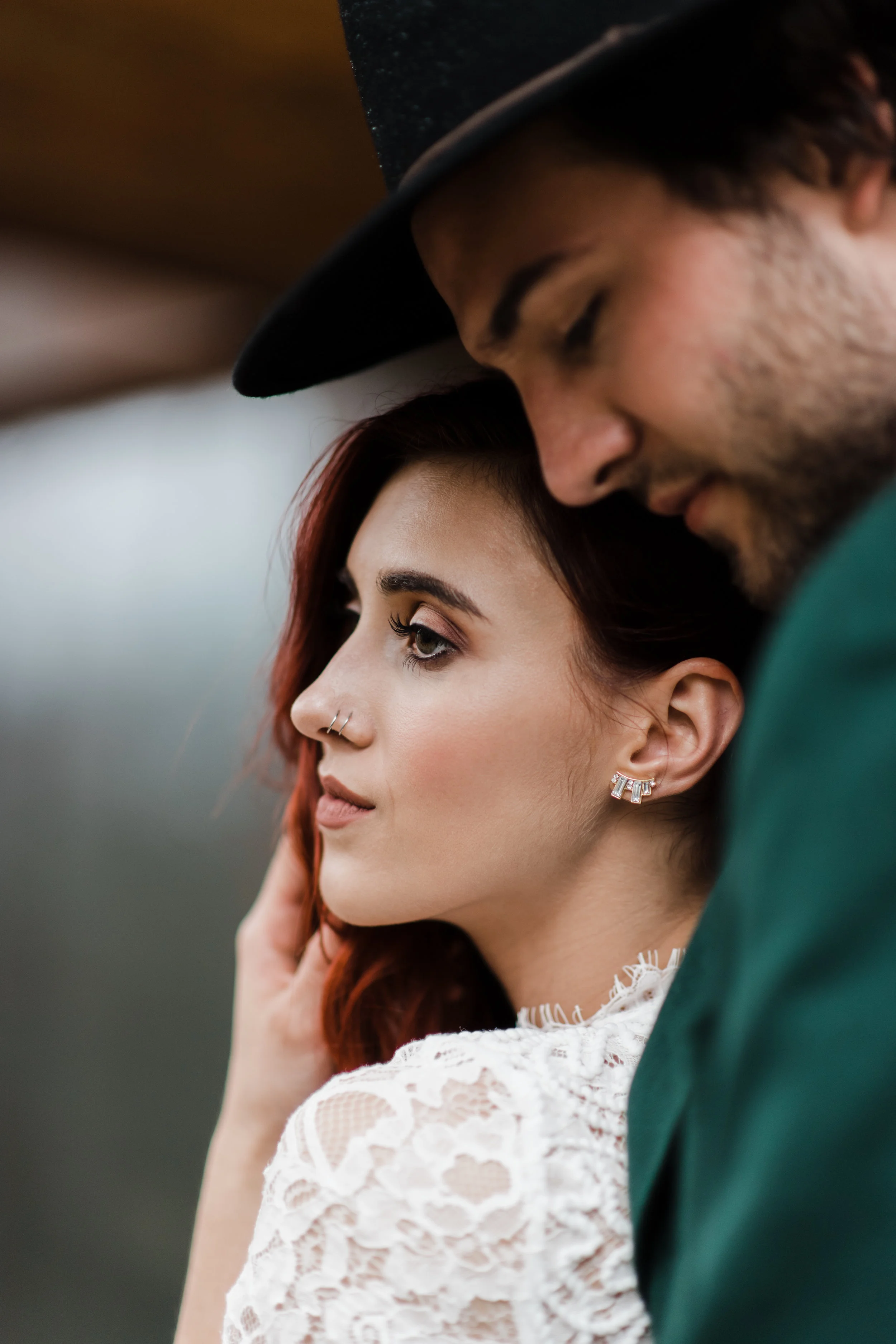 Bride with long curly eyelashes and nose rings and rectangular earring running hand through her hair and staring off into the distance.
