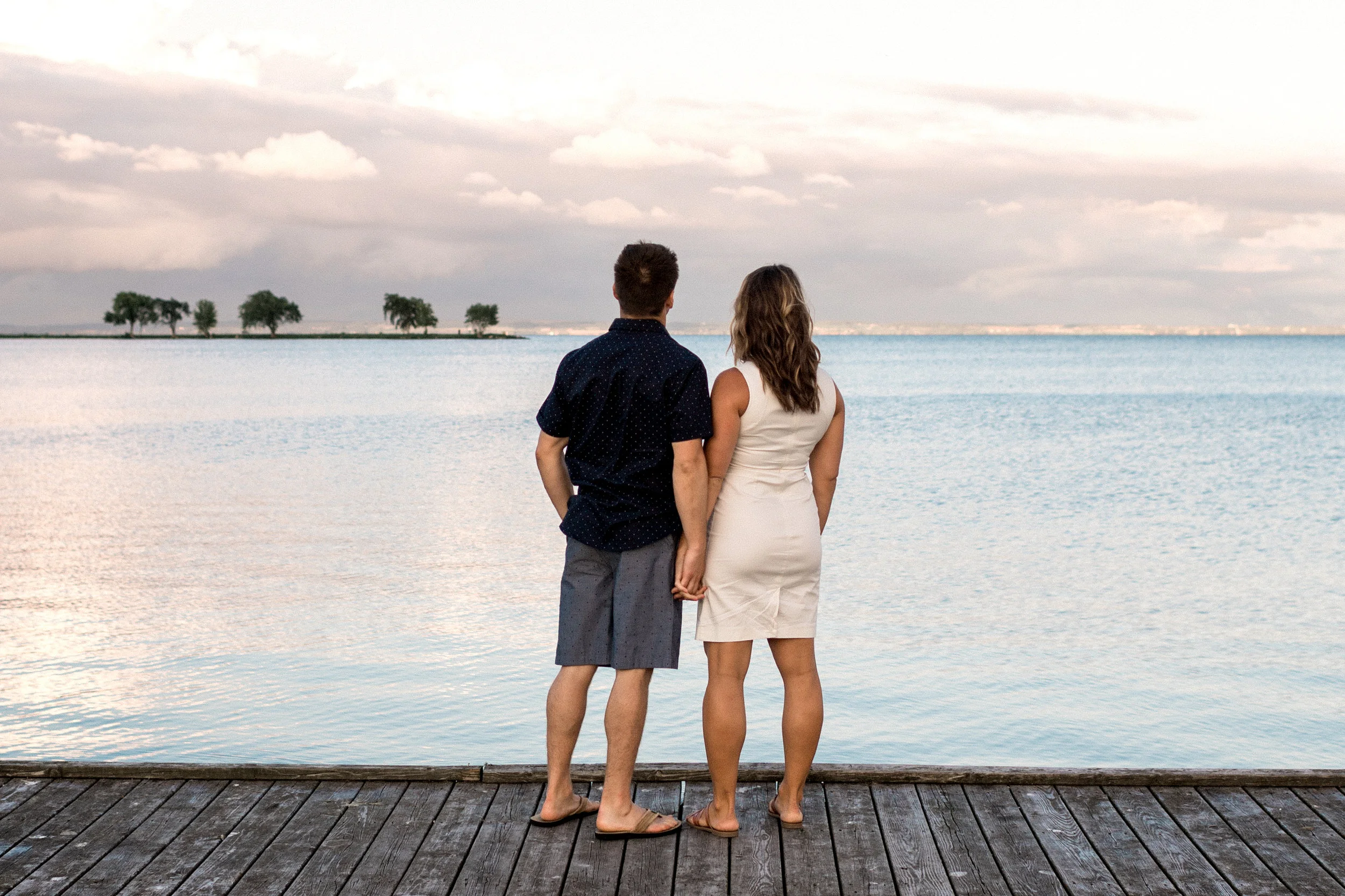 Engaged couple holds hands standing on a dock overlooking Lake Winnebago in Wisconsin.