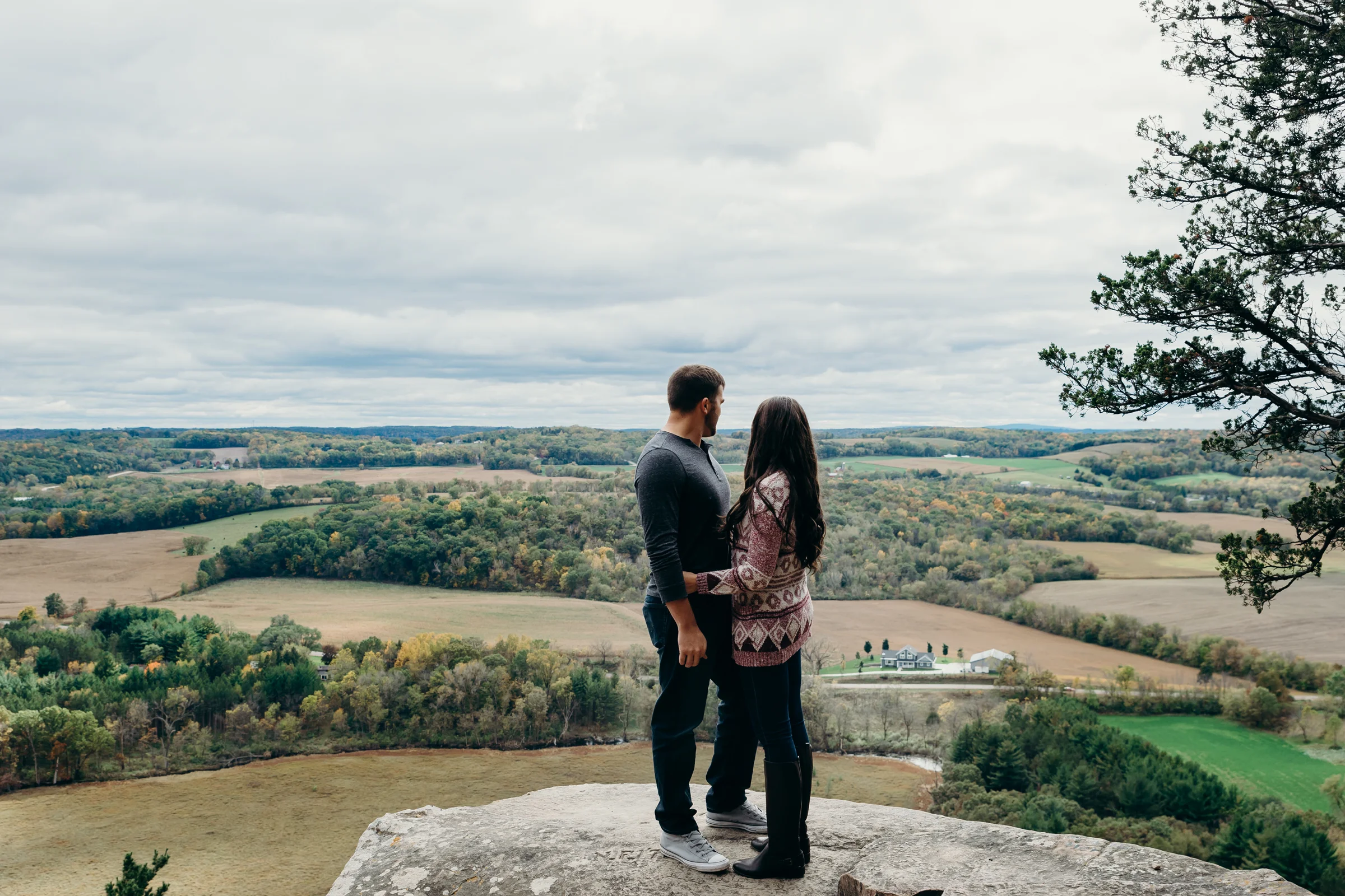 Engaged couple stands on top of a rock overlooking Lodi, WI at Gibraltar Rock State Natural Area.