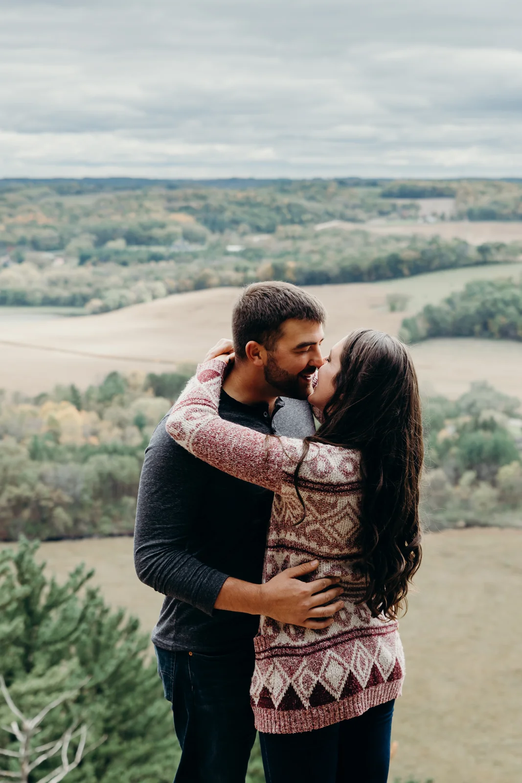 Engaged couple kisses in front of a scenic background.