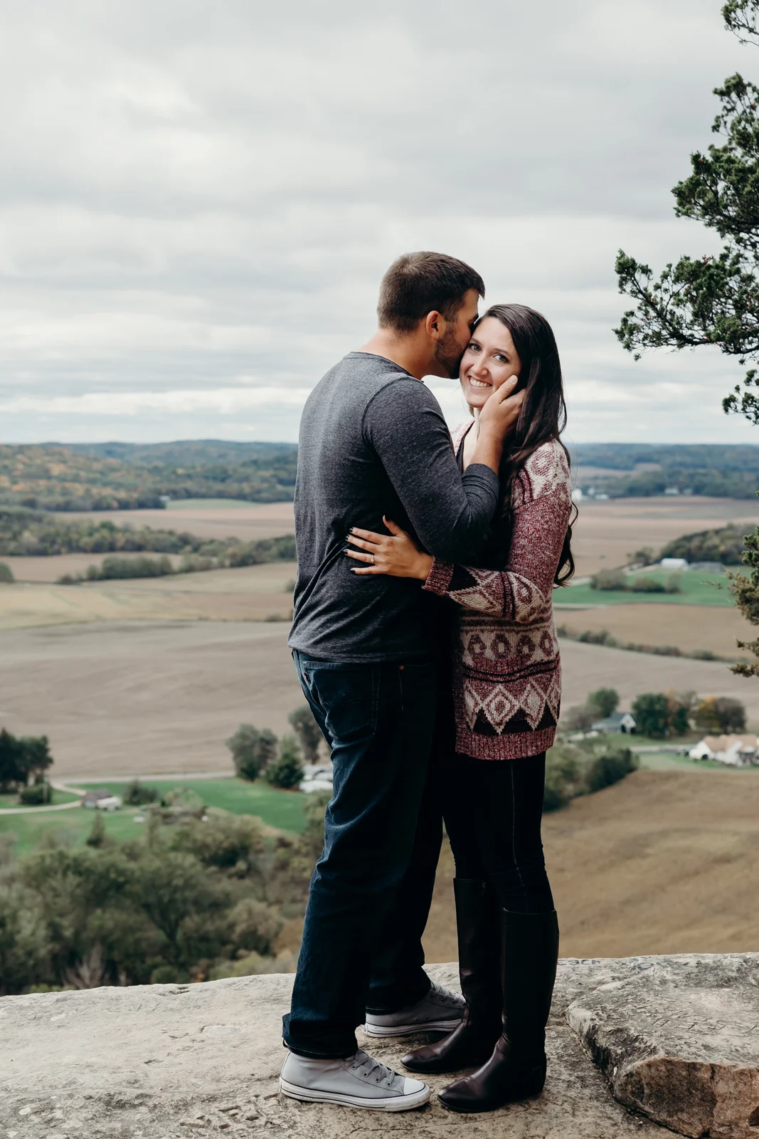 Woman smiles as her fiancé kisses her cheek.