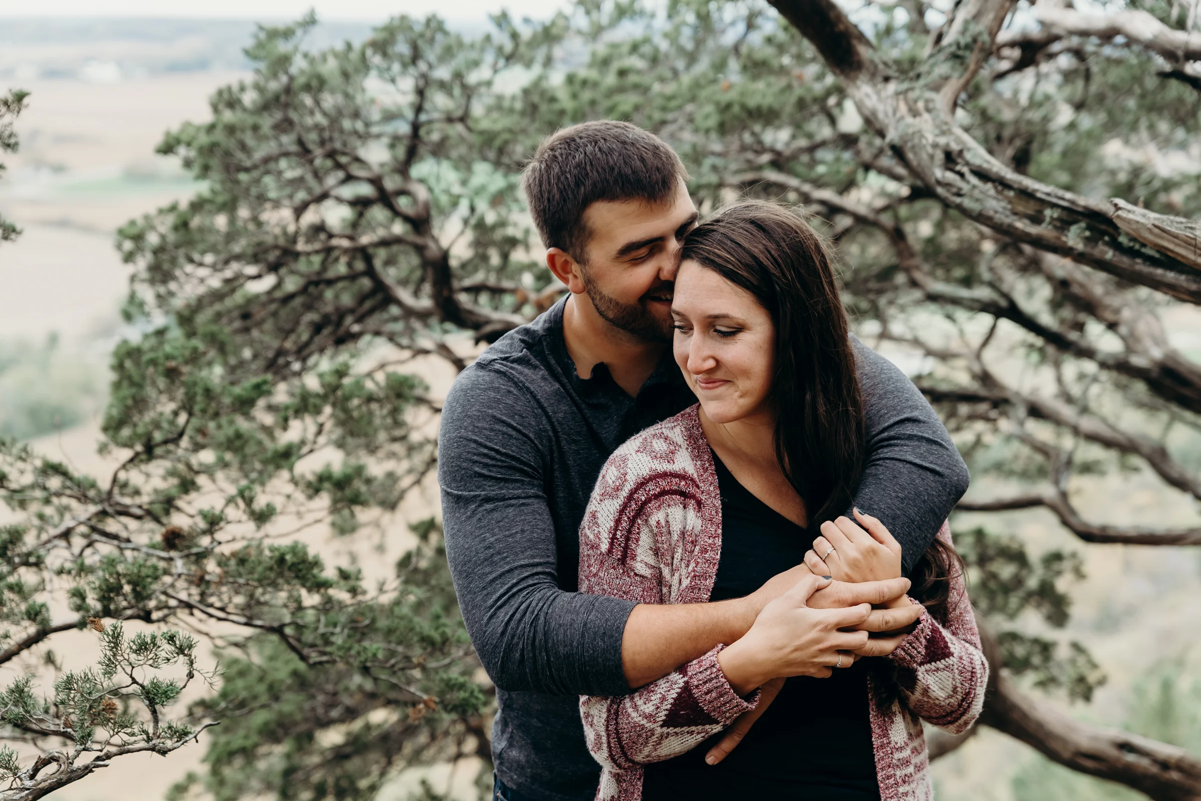 Man wraps his arms around his fiancé and giggles into her hair.
