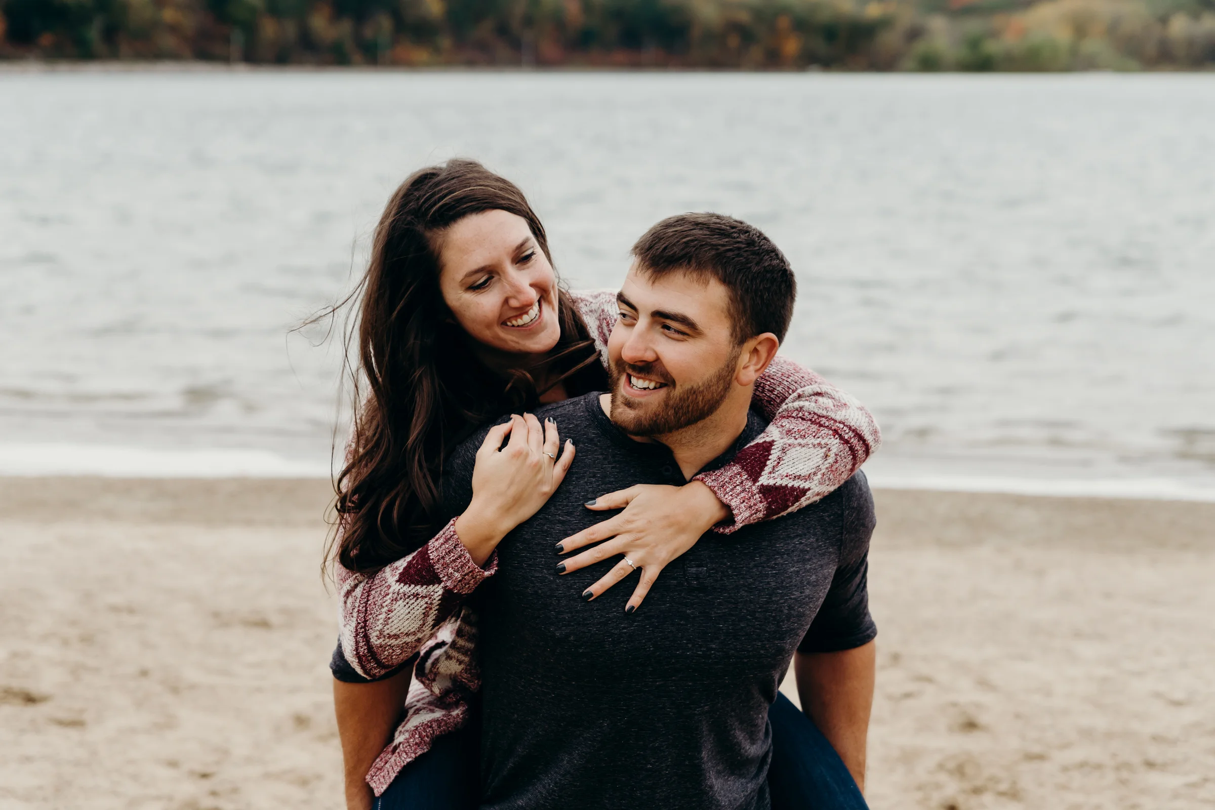 Engaged couple smile at each other while the man gives his fiancé a piggy back ride.