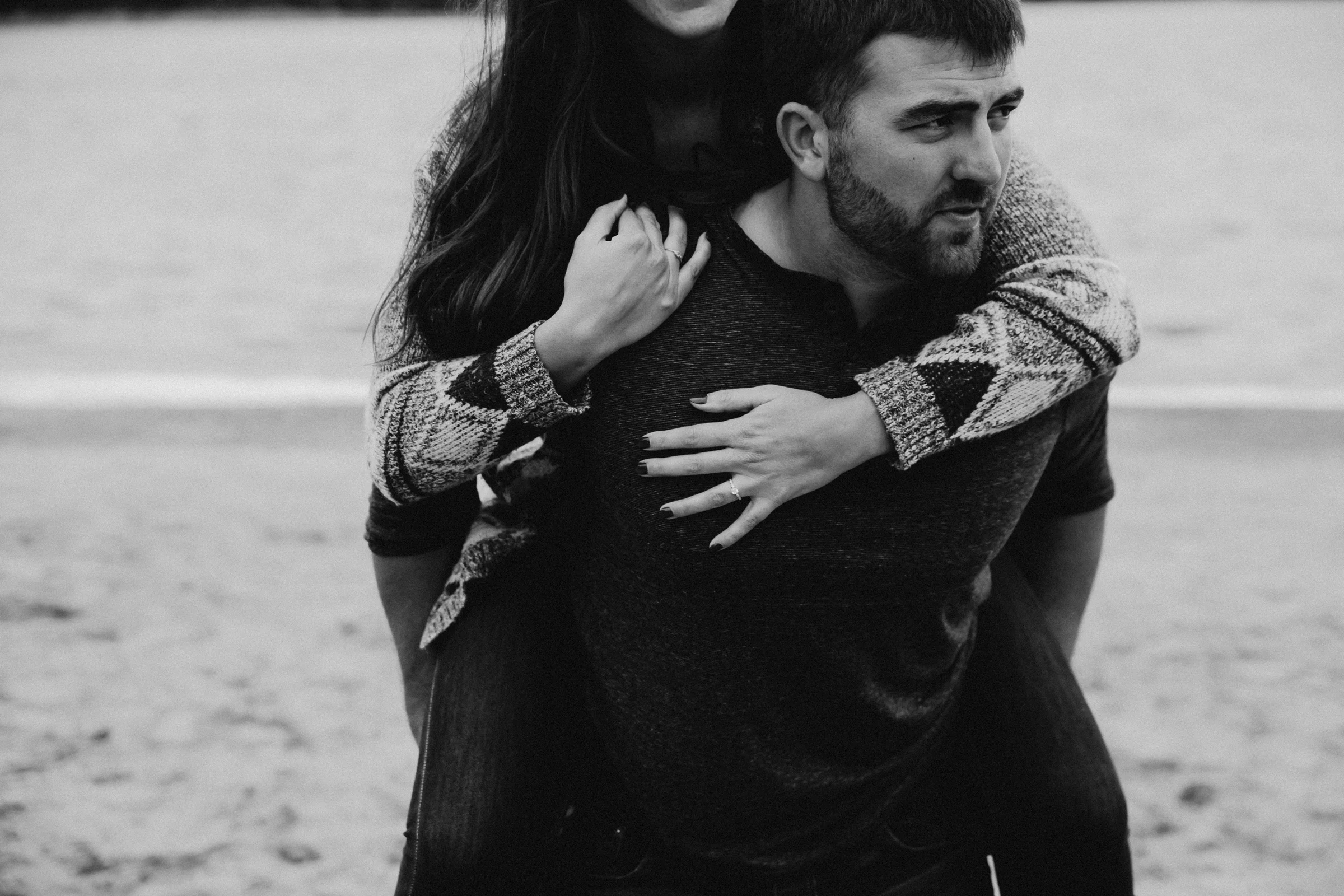 Man looks serious as he carries his fiancé across the beach.