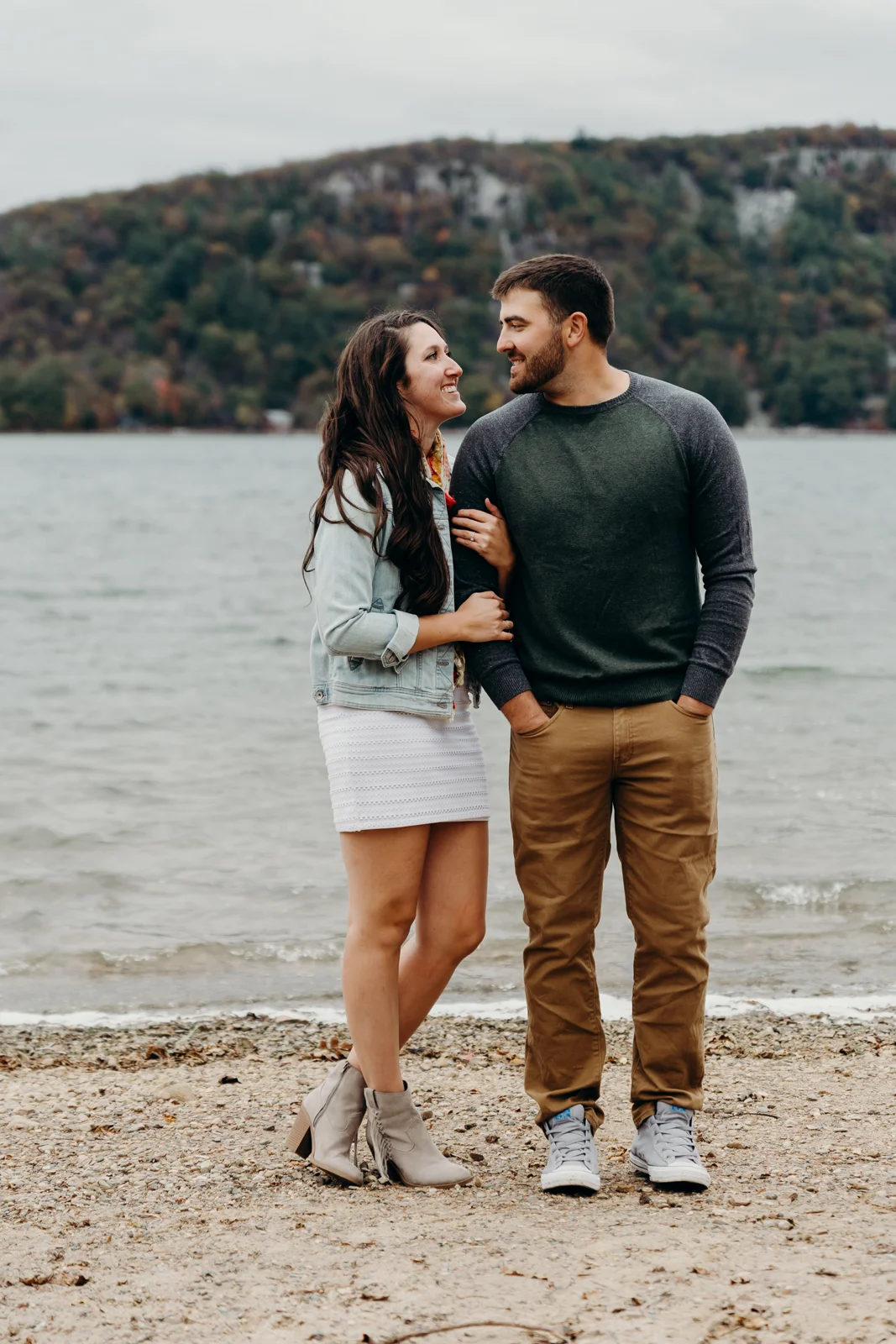 Engaged couple stand next to each other and smile at each other.