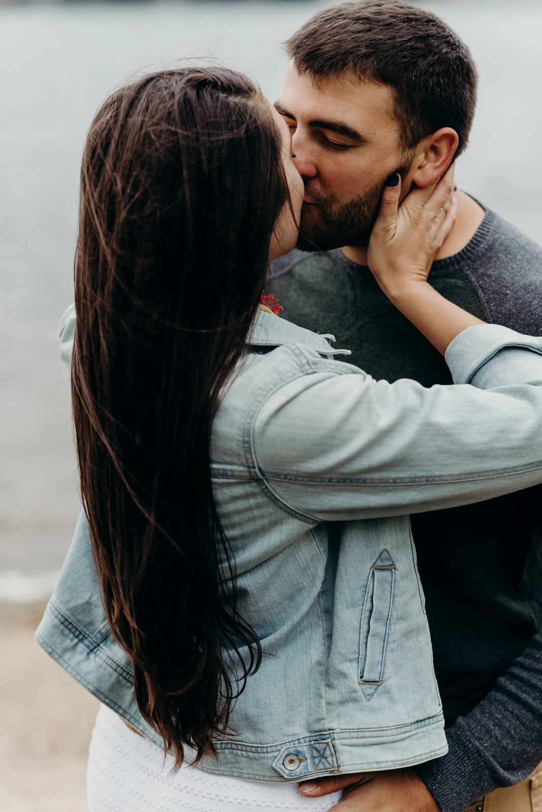 Woman holds her fiancé's face and kisses him.