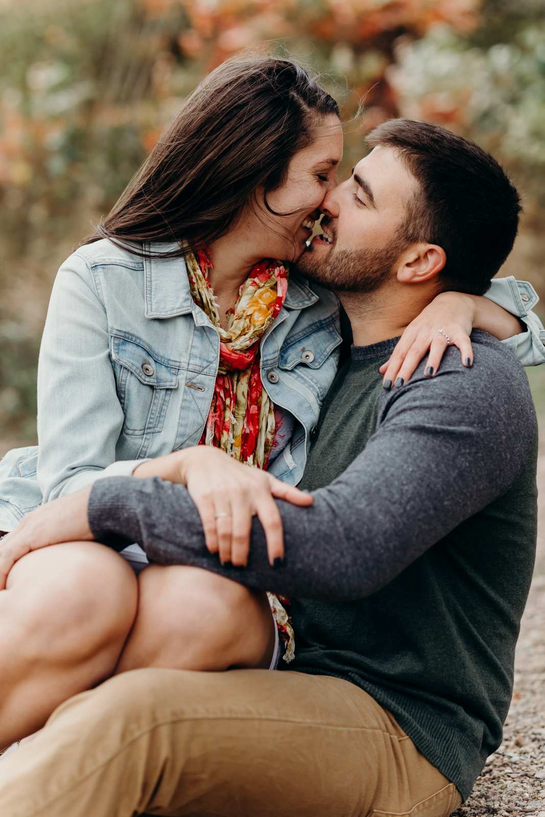 Woman sits on her fiancé's lap, and they lean in to kiss each other.